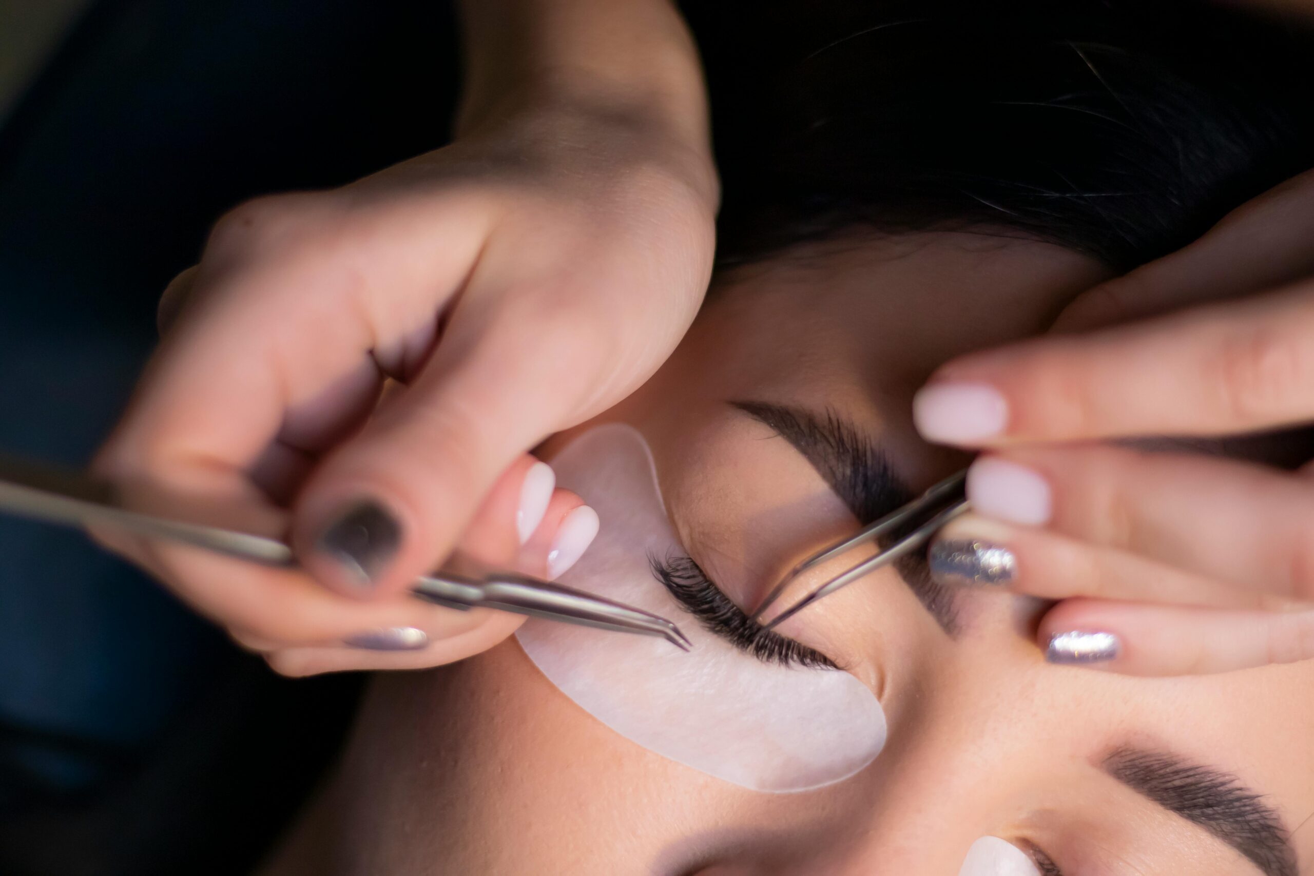 Detailed view of a beautician applying eyelash extensions to a woman's eyes.